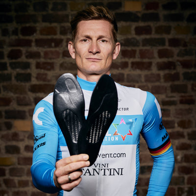 A professional cycling athlete holding the pair of SOLESTAR insoles as if they were cards in their hand.